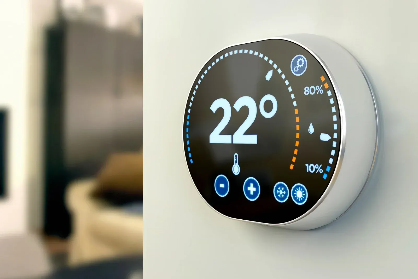 Smart thermostat displaying 22°C on a white wall, with a blurred living room in the background.
