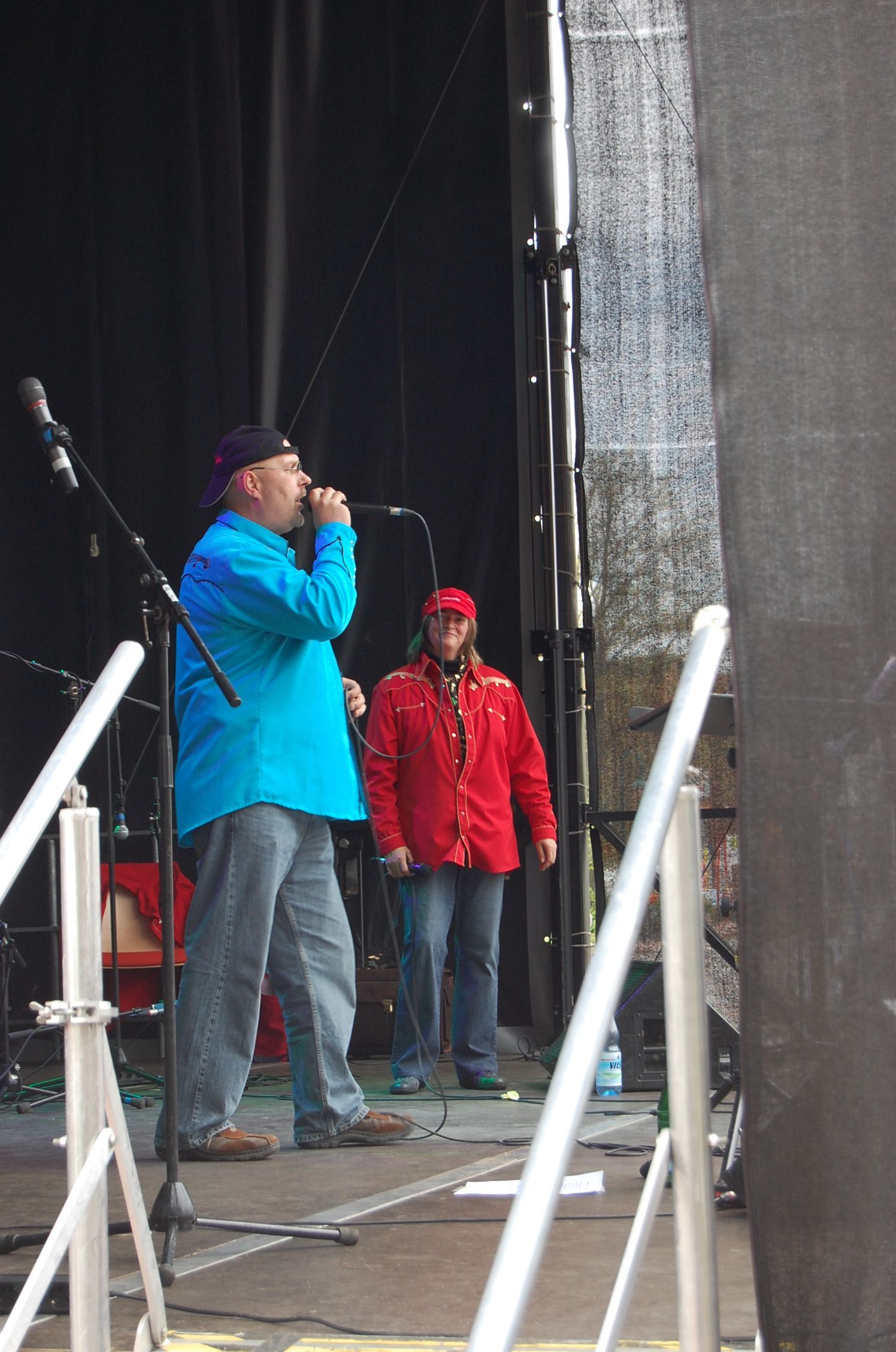Ein Mann in blauem Hemd singt auf der Bühne, ein anderer in roter Jacke steht dahinter.