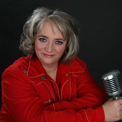 Frau in rotem Hemd lächelt und hält ein Vintage-Mikrofon vor dunklem Hintergrund.