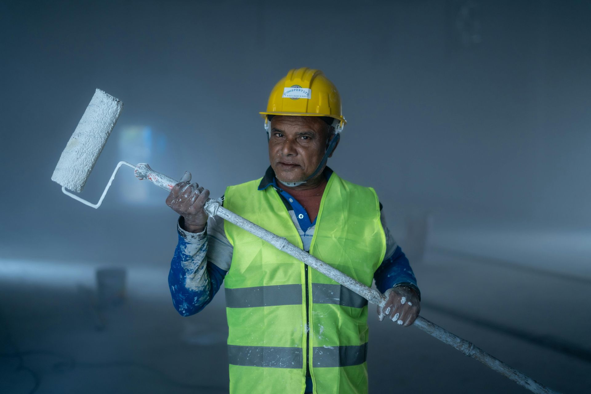 Construction worker in yellow hard hat and safety vest holding a paint roller in a dim tunnel