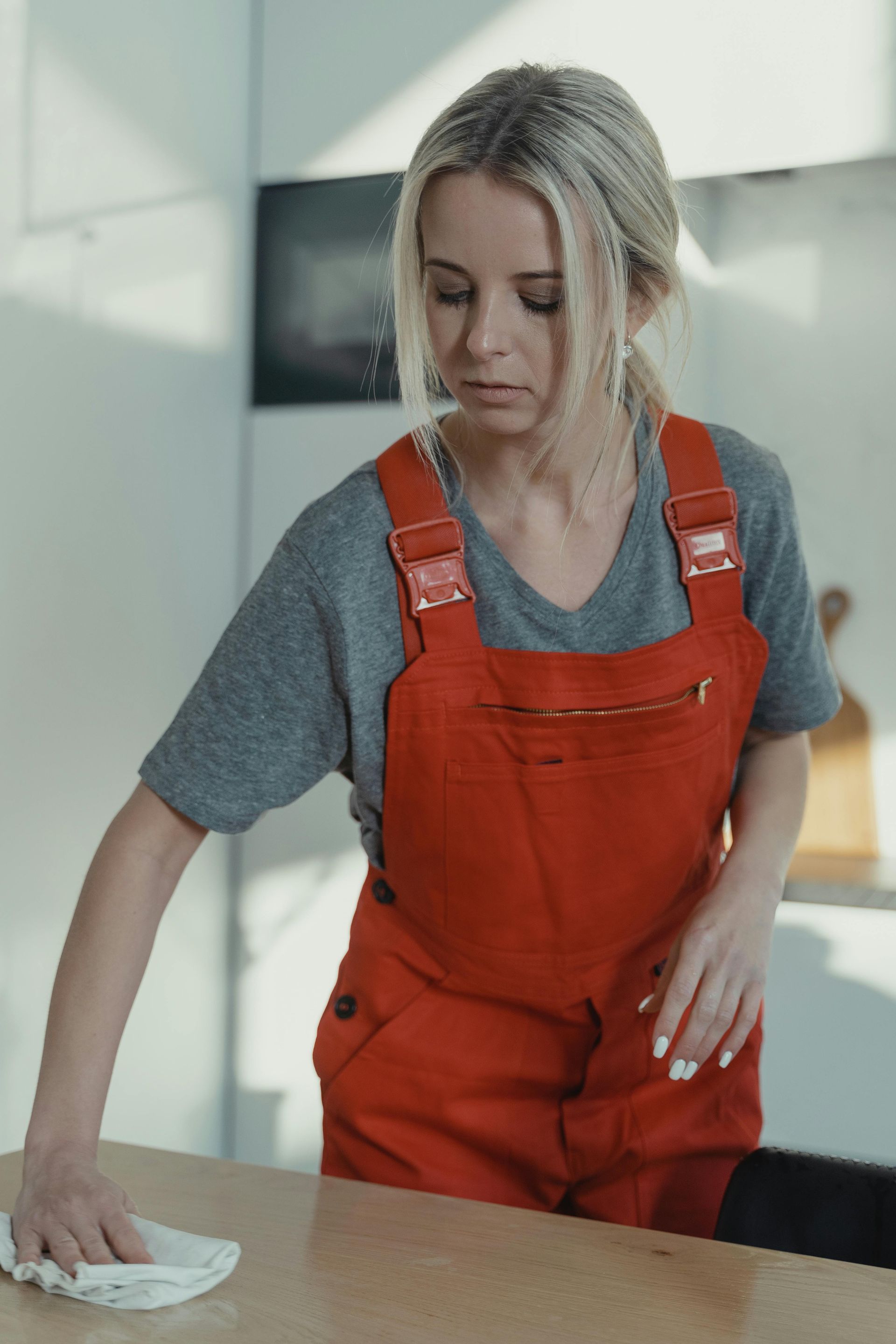 Woman in orange overalls wiping a countertop in a bright kitchen