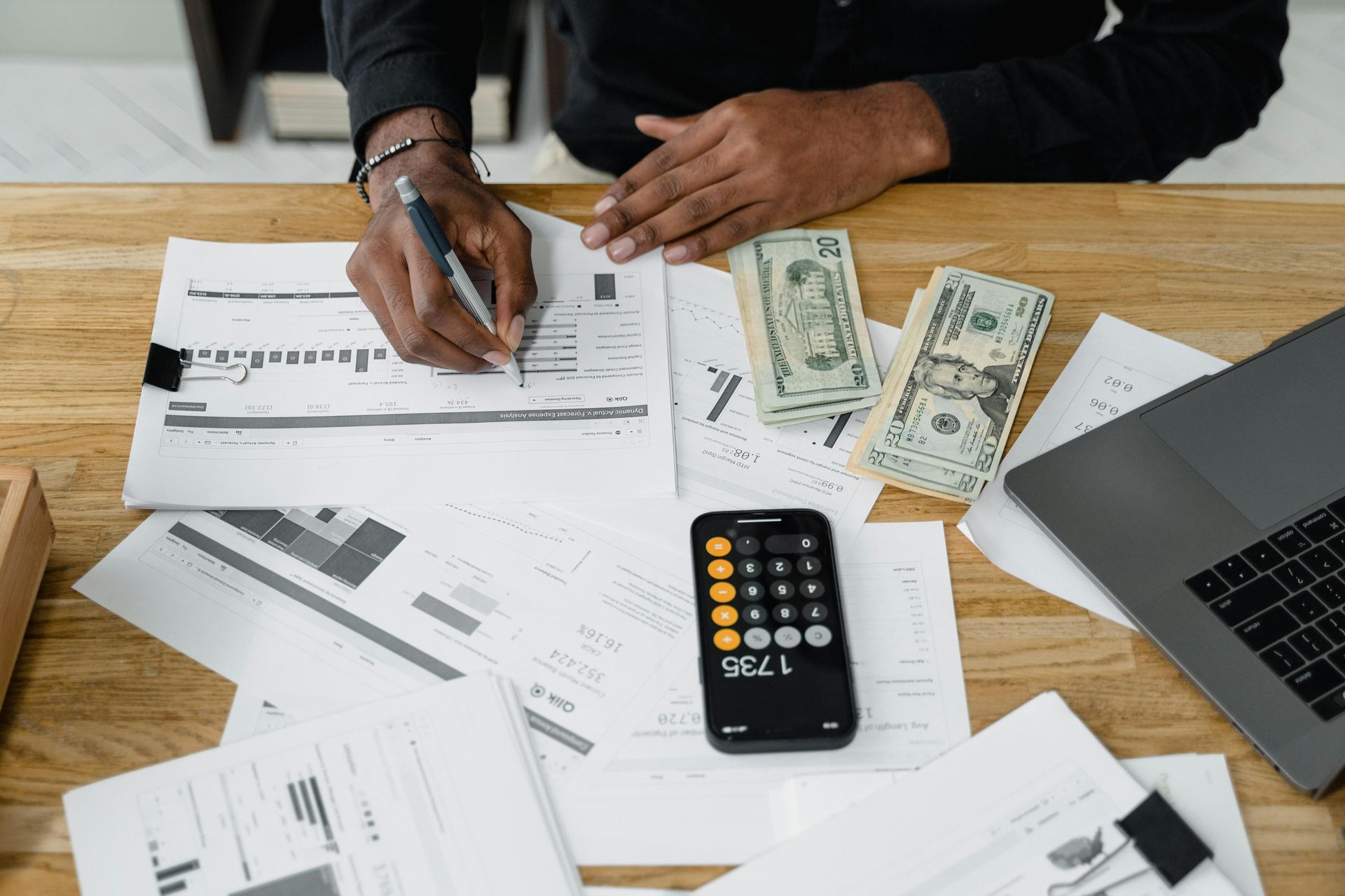 Person reviewing financial documents at a desk with cash, calculator, and laptop