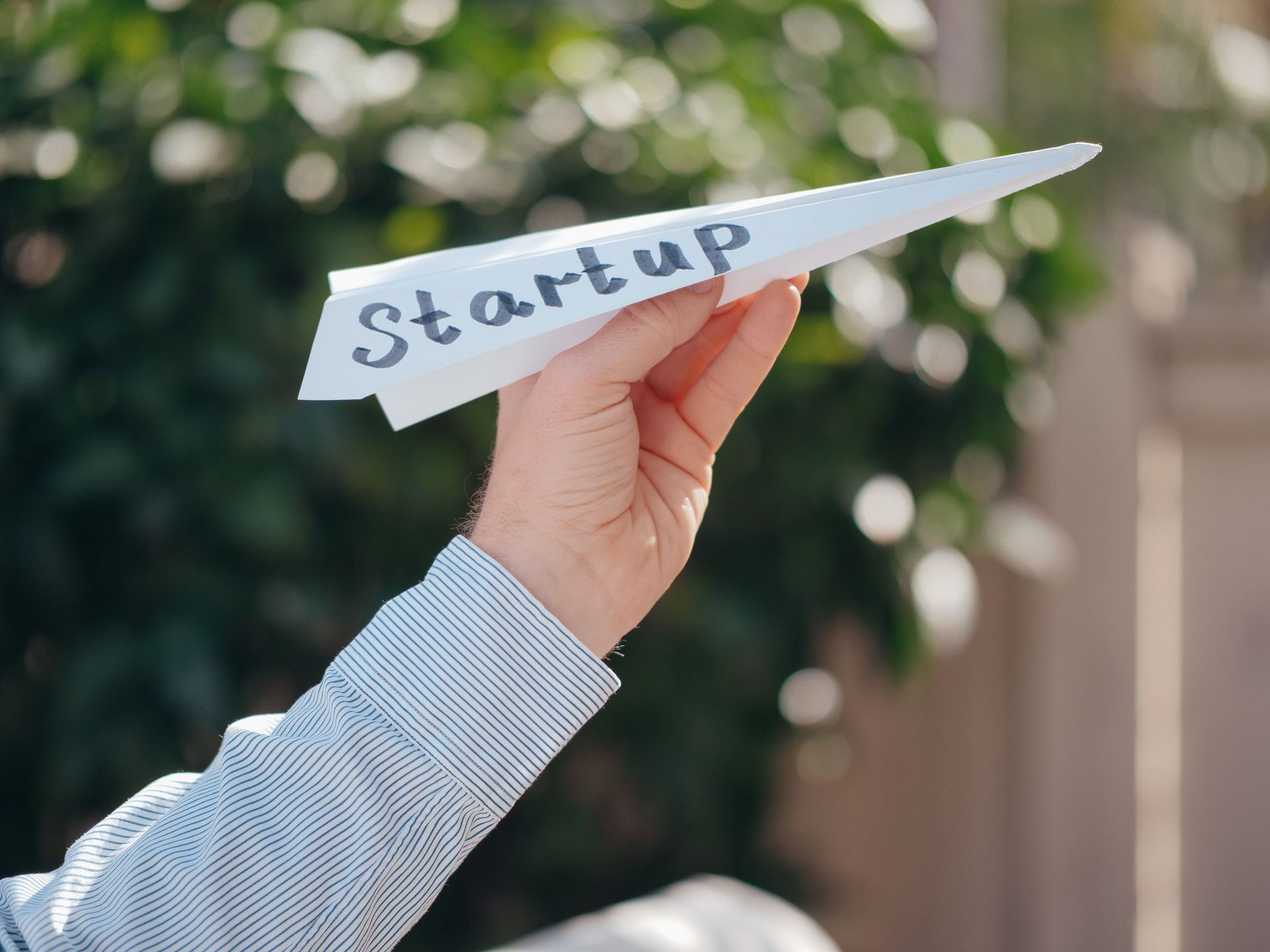 Hand holding a paper airplane labeled “Start up” against a blurred outdoor background