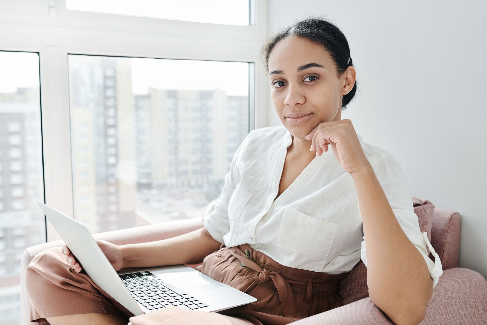 Person sitting on a sofa using a laptop beside a bright window