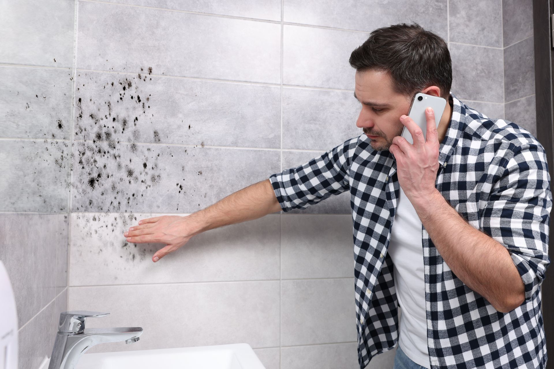 Person inspecting black mold on bathroom tiles while making a phone call near a sink. Person inspecting black mold on bathroom tiles while making a phone call near a sink.