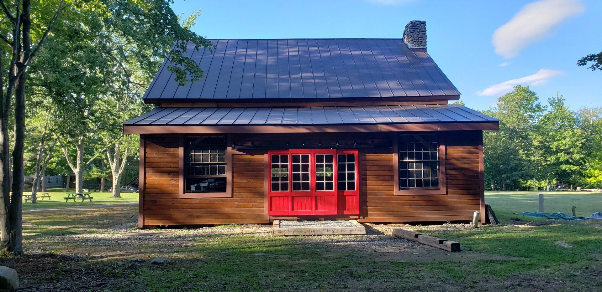A small wooden house with a red door is sitting in the middle of a grassy field.