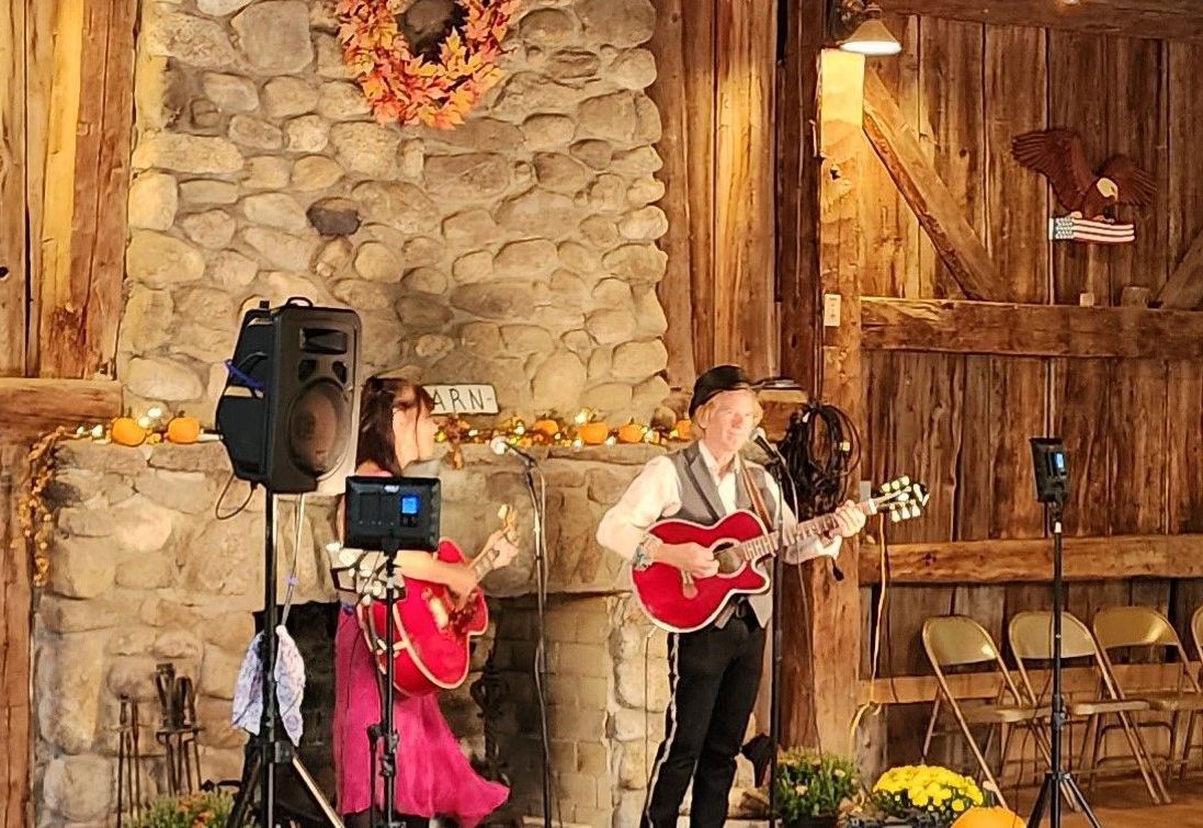 A man and a woman are playing guitars in front of a stone fireplace.