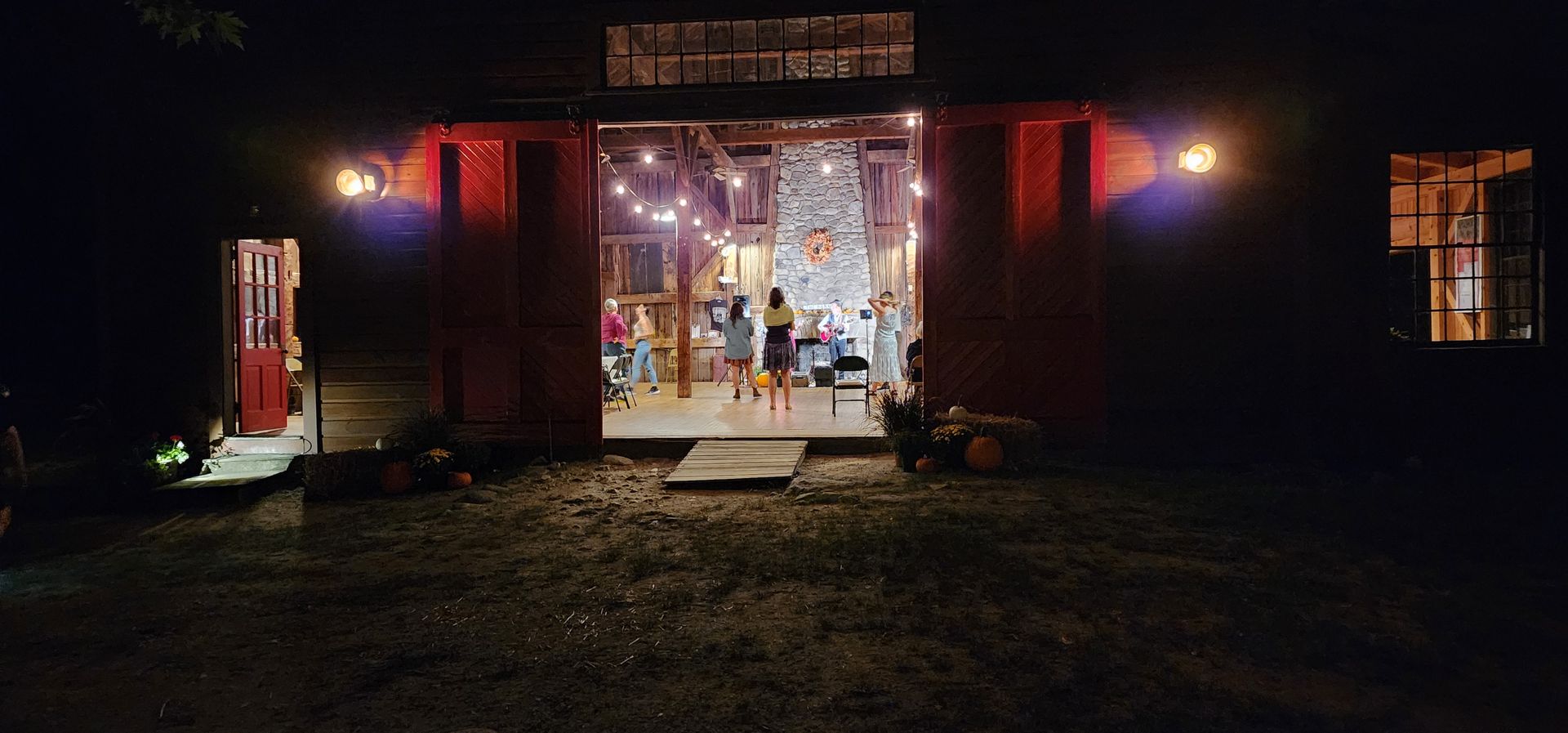 A group of people are standing in front of a barn at night.