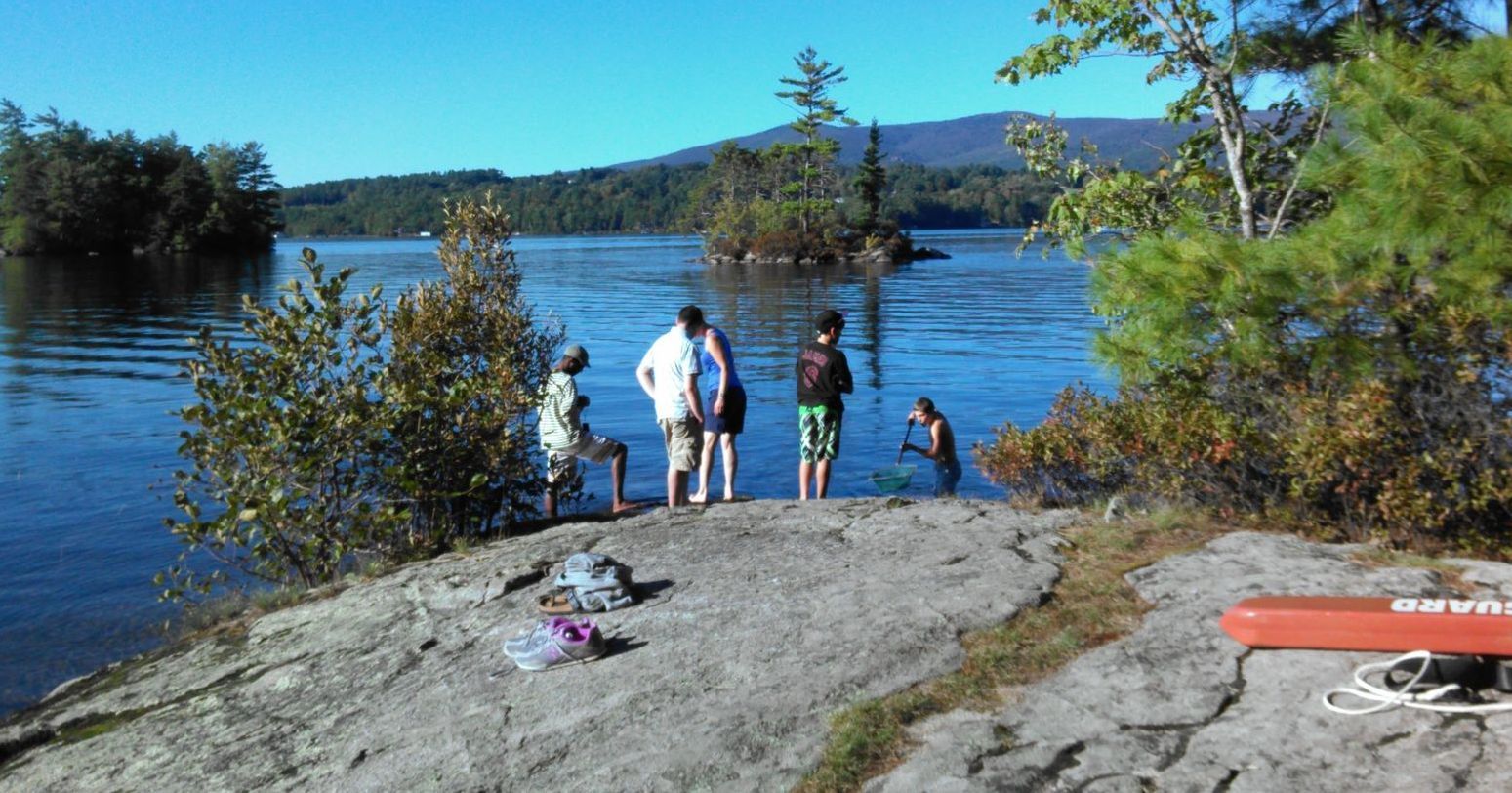 A group of people are standing on a rock near a lake.