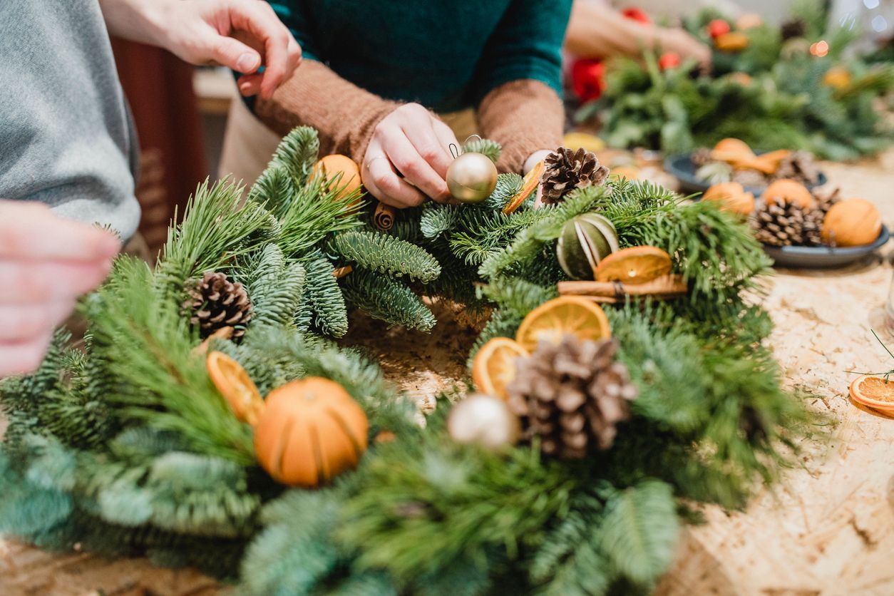 A group of people are making a christmas wreath on a table.