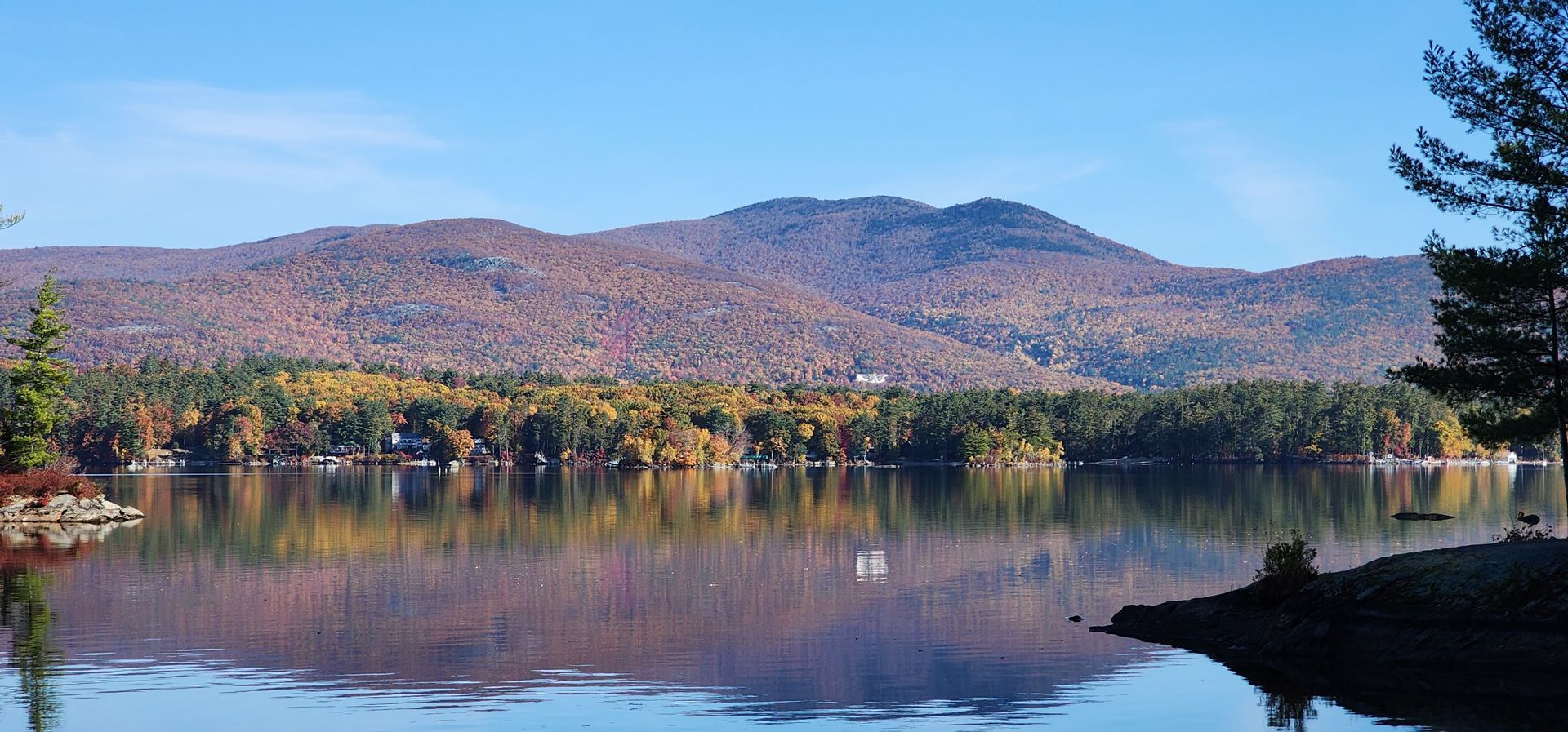 A lake reflects the colorful autumn foliage and mountains under a clear blue sky.