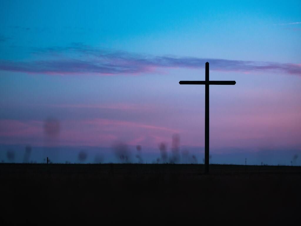 Silhouette of a cross against a blue-purple sunset sky over a dark horizon