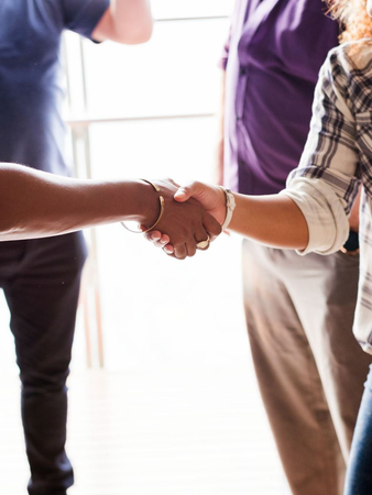 Two people shaking hands in a bright indoor setting, with others standing nearby