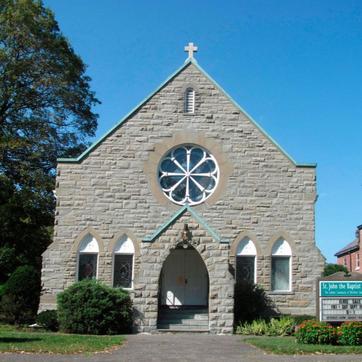 Small stone church with arched windows and a cross, seen front-on under a blue sky.