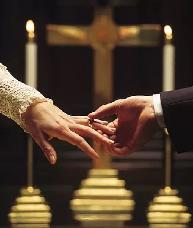 Hands exchanging rings before a church altar with candles and a cross in the background