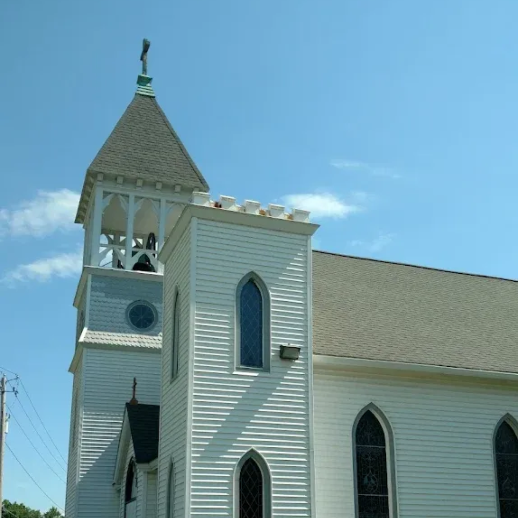 White church steeple and side facade with arched windows under a clear blue sky