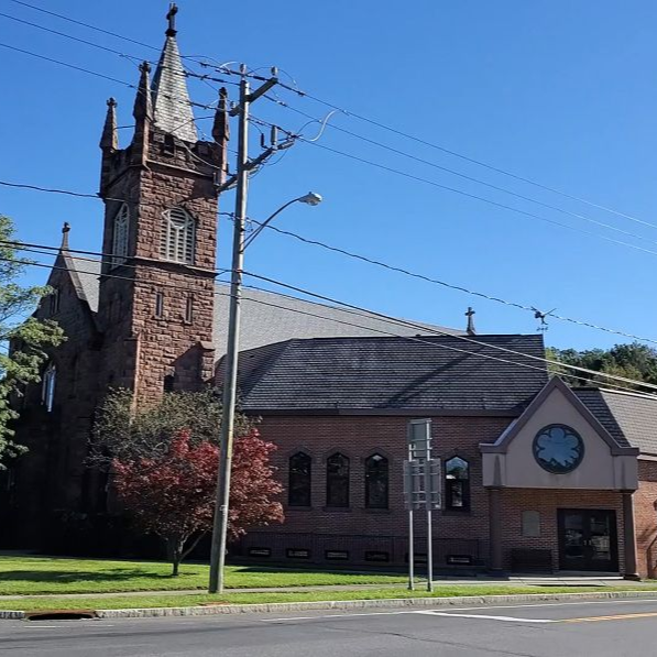 Stone church with tall steeple and brick annex on a sunny street corner under a clear blue sky.