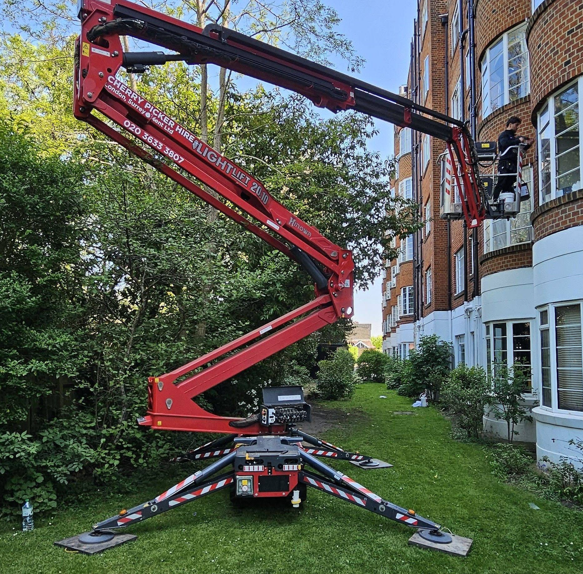 A red crane is sitting in front of a brick building.