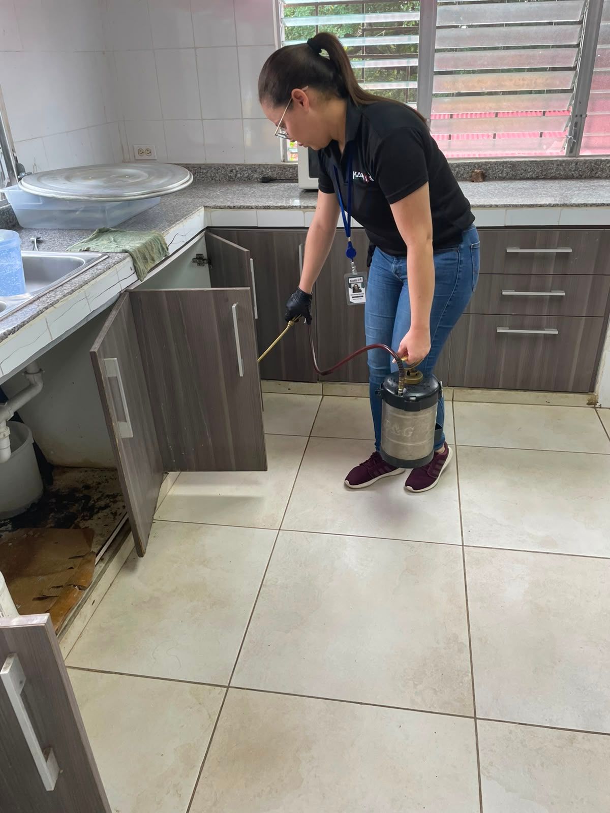 Una persona con traje protector rocía desinfectante en una cocina con un pulverizador manual.