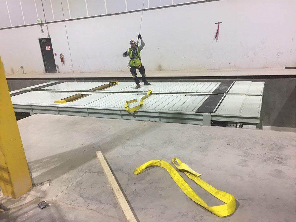 Worker in safety harness on elevated platform, pulling on rope. Yellow straps and concrete surroundings.