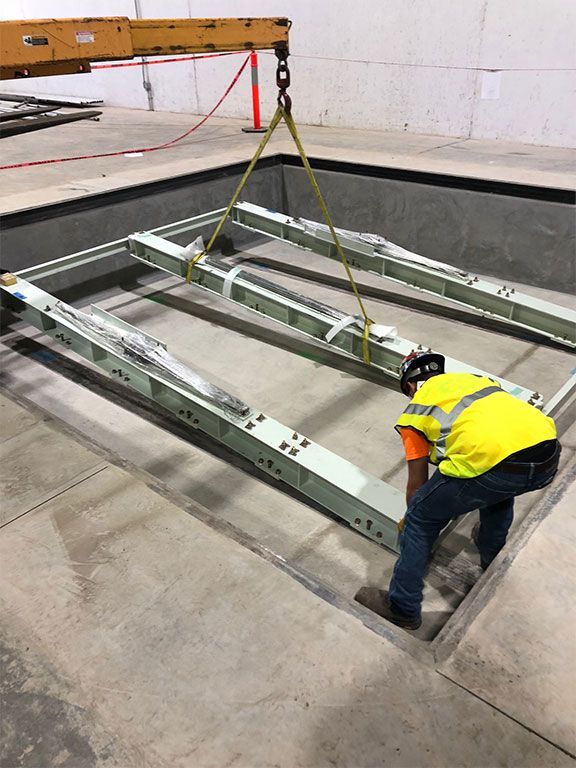 Worker in safety vest guides a metal frame being lifted by a crane into a recessed area.