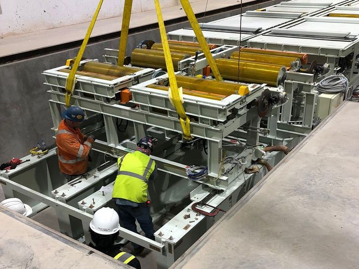 Robots assembling a silver car body in an automated factory; red and yellow robotic arms.