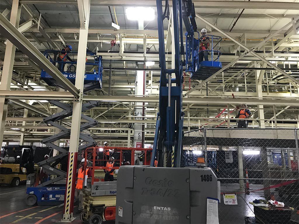 Workers in aerial lifts, inside a factory, installing or repairing overhead equipment.