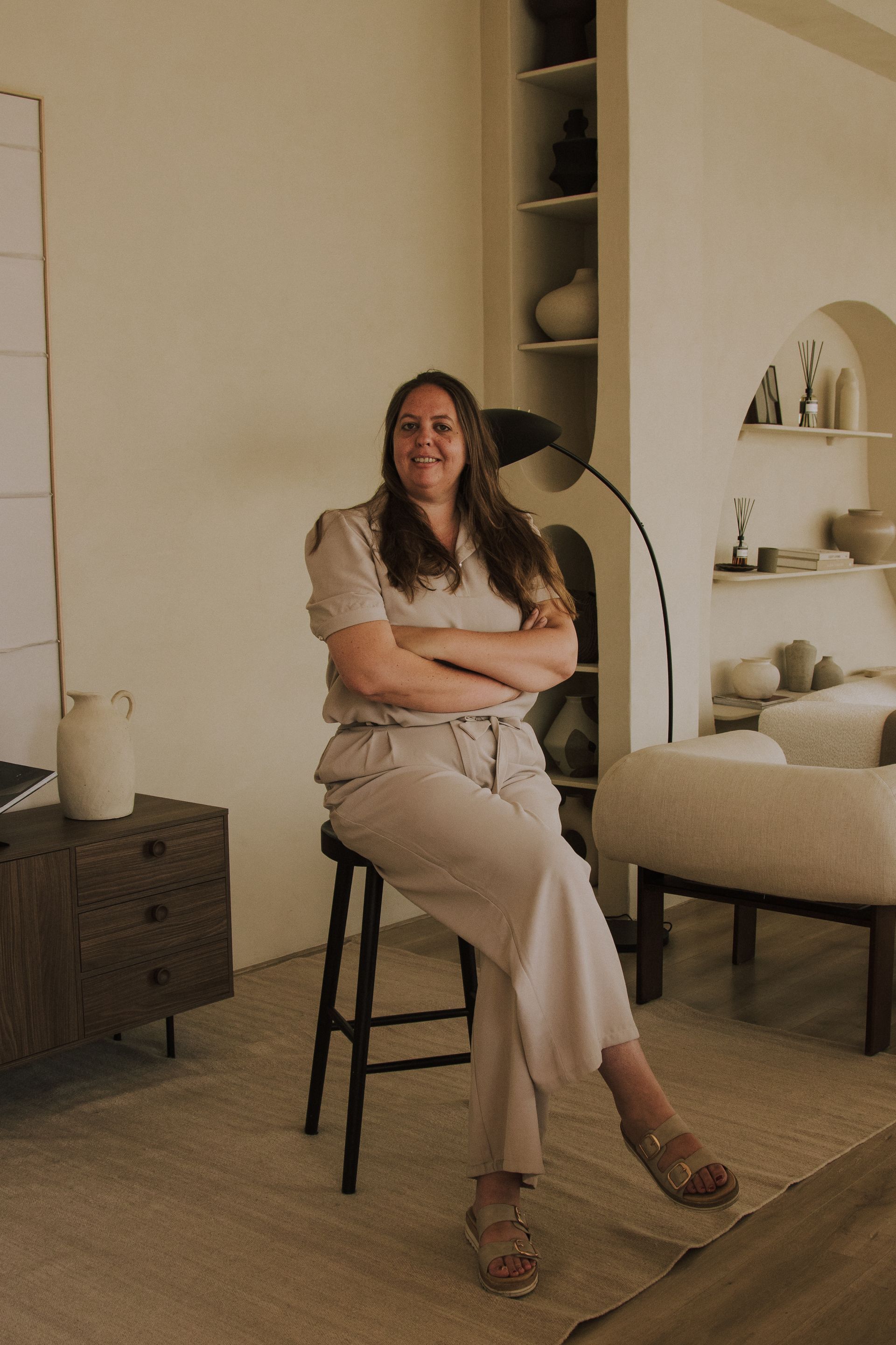 Woman sitting on a chair in a warm, minimalist room with neutral decor and arched shelves