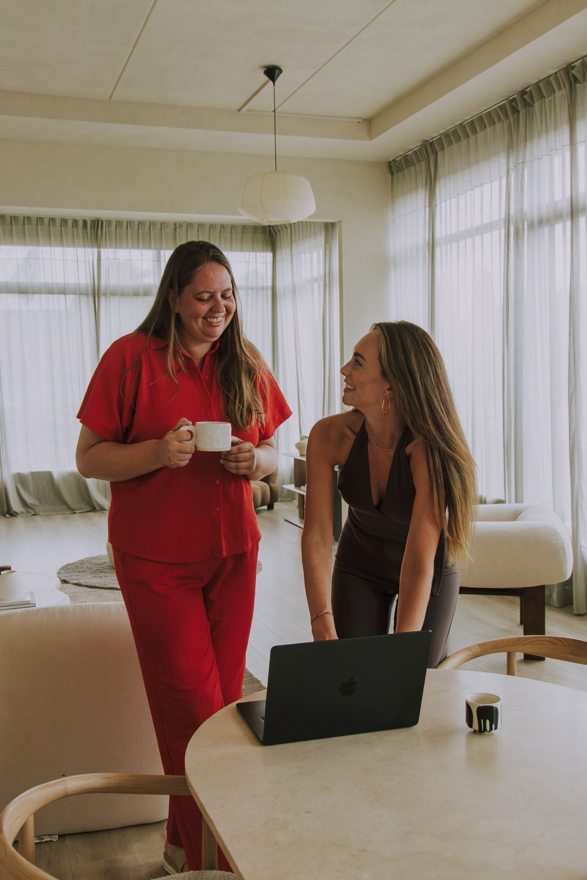 Two women talking beside a table with a laptop in a bright room