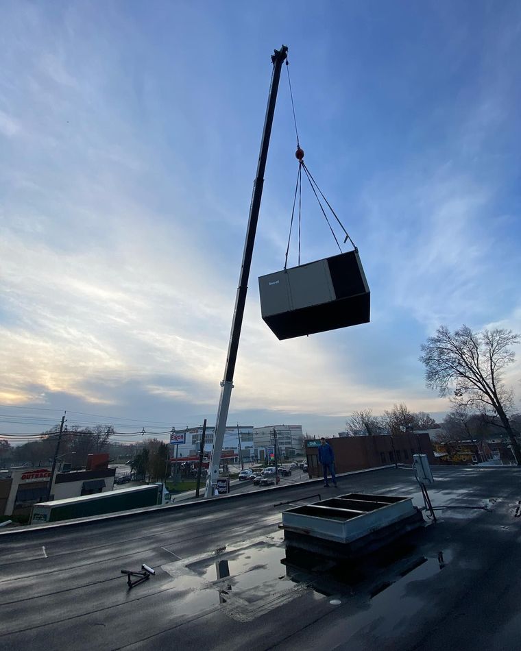 Crane lifting a large black container over a rooftop at dusk under a blue sky