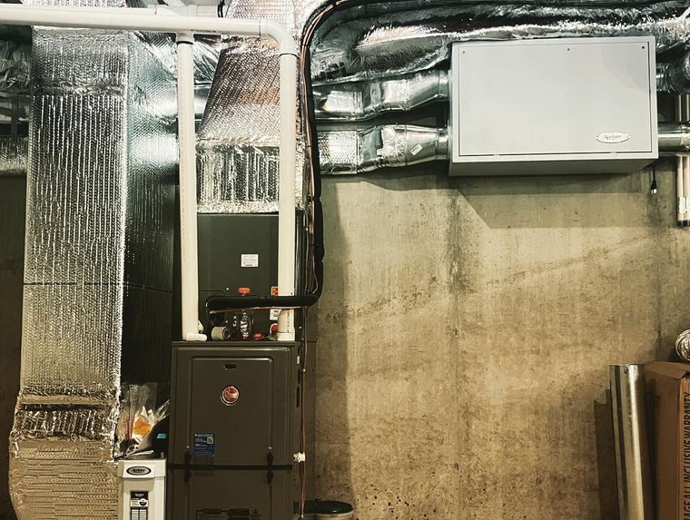 Basement utility room with HVAC units, exposed ductwork, and a concrete wall