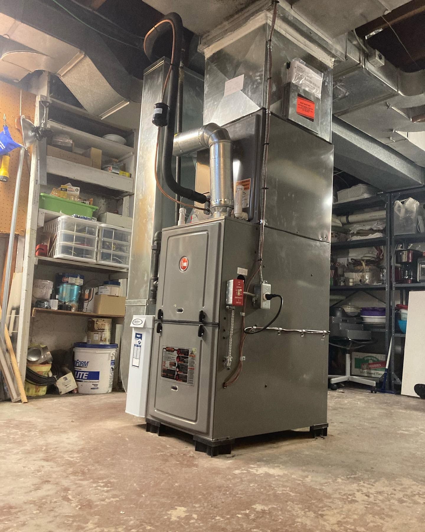 Large gray industrial machine in a basement workshop with exposed pipes and storage shelves.
