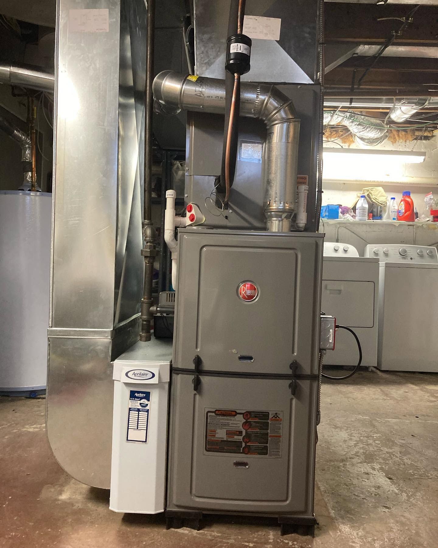 Gray furnace and white water heater in a basement utility room with exposed pipes and ductwork