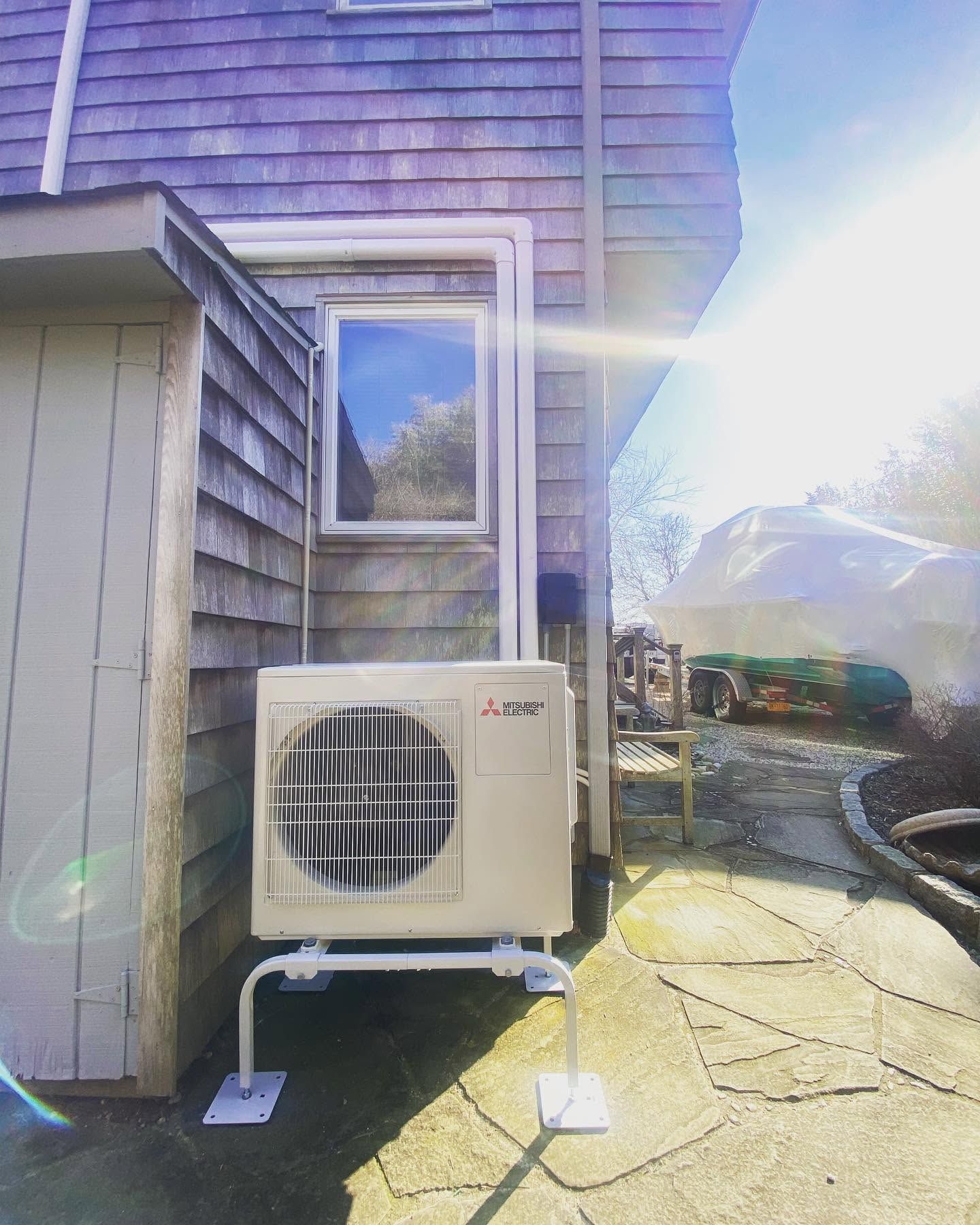 Outdoor HVAC unit beside a house, with bright sun glare and a stone patio in the foreground