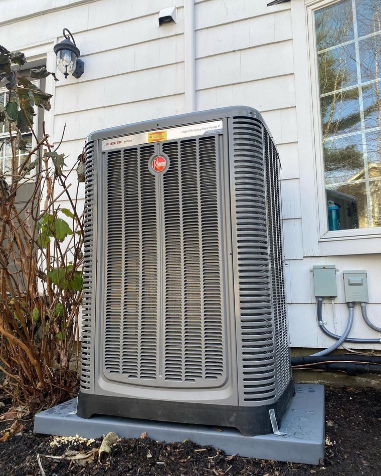 Outdoor HVAC unit beside a house wall, with white siding and a nearby window.