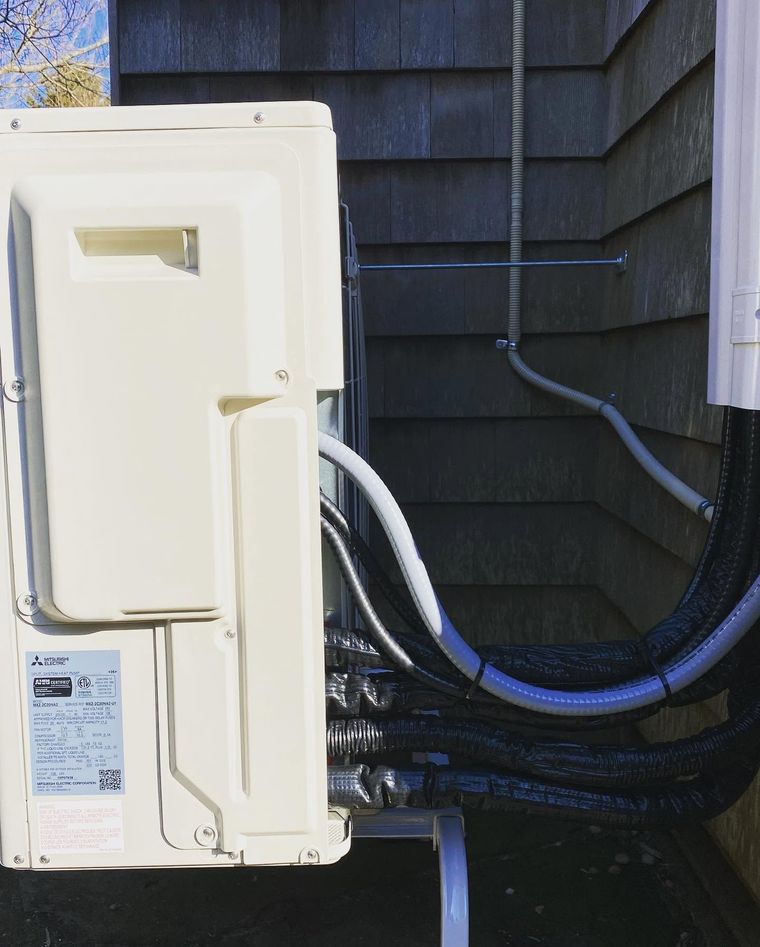 Exterior utility panel with white cover and bundled cables beside dark house siding