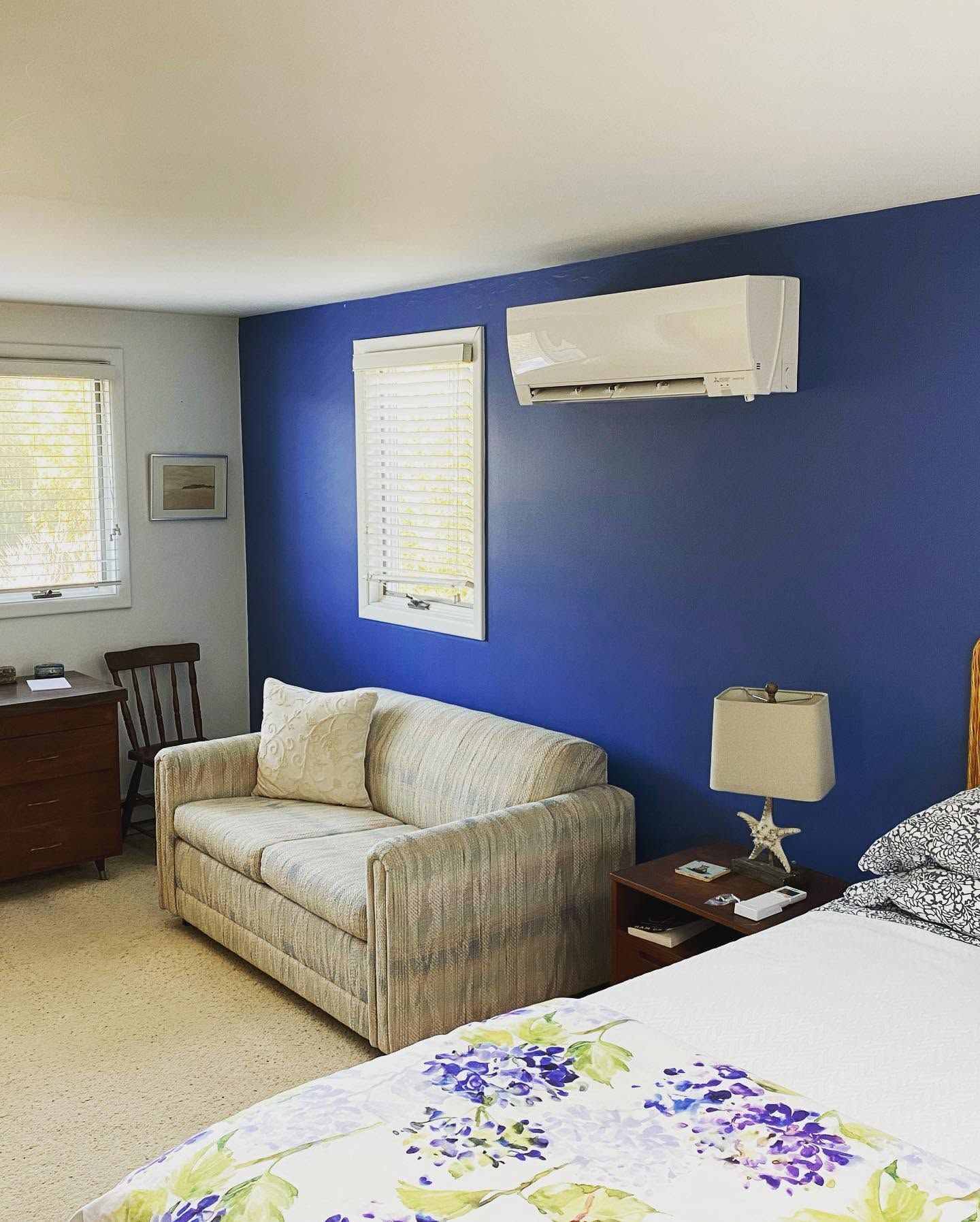 Bedroom with blue accent wall, bed, sofa, window, and wall-mounted air conditioner