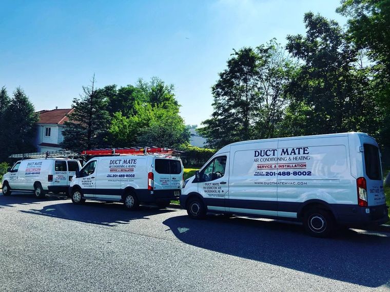 White service vans parked on gravel near trees and a building, with “DUCT MATE” visible on one van.