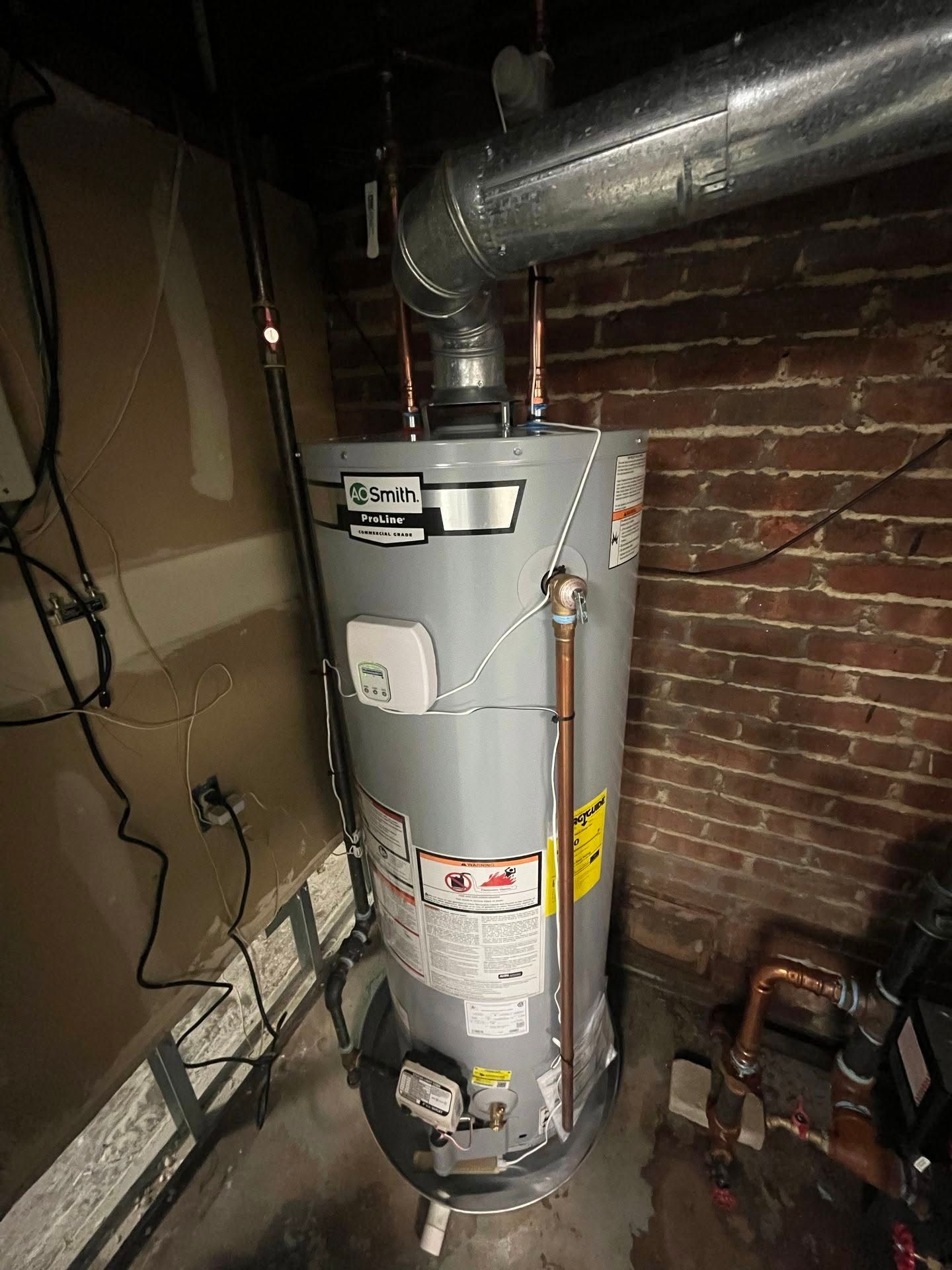 Basement water heater with metal ductwork beside a brick wall and exposed pipes