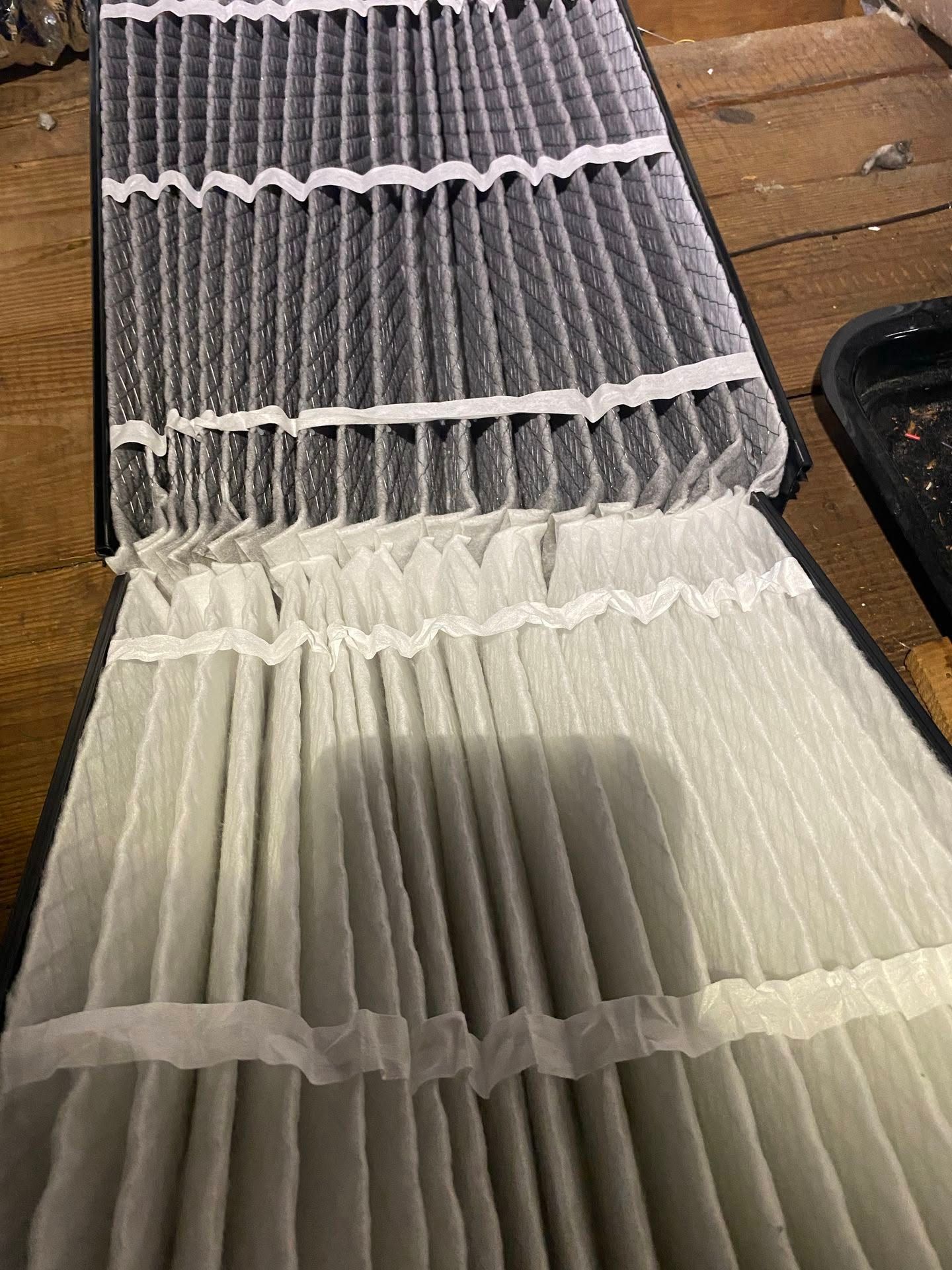 Opened pleated accordion-style filter with gray and white pleats on a wooden surface