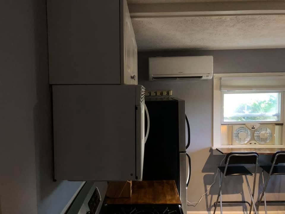 Small apartment kitchen and dining nook with gray cabinets, black fridge, table, chairs, and window air conditioner