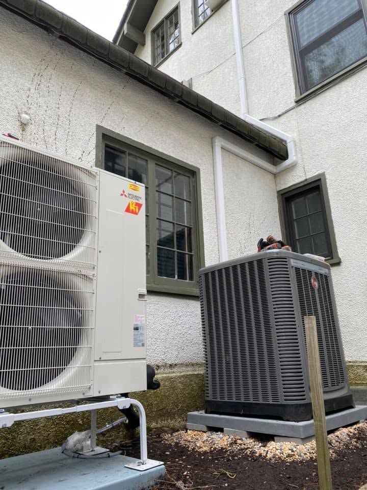 Outdoor HVAC units beside a white house, with one large condenser in the foreground.