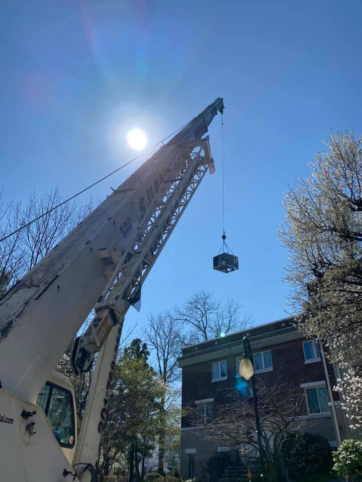 Crane lifting a load beside a brick house under a bright blue sky