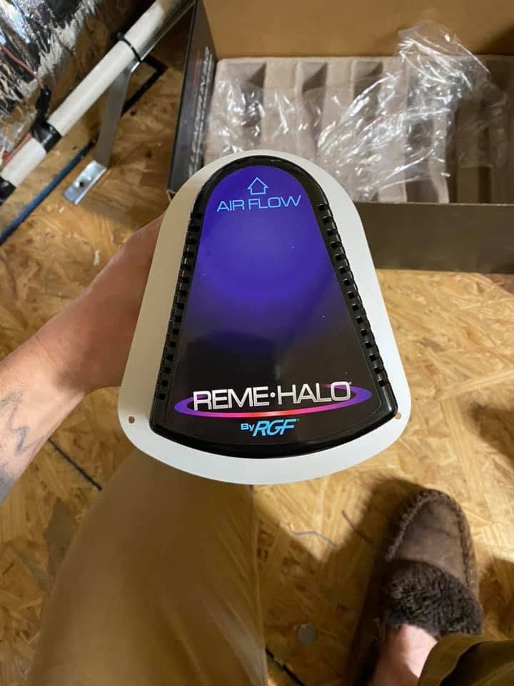 Hand holding a purple and black RemE-Halo air purifier box in a storage area