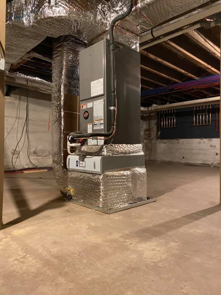 Basement HVAC unit wrapped in silver insulation beside exposed ductwork and ceiling beams Basement HVAC unit wrapped in silver insulation beside exposed ductwork and ceiling beams