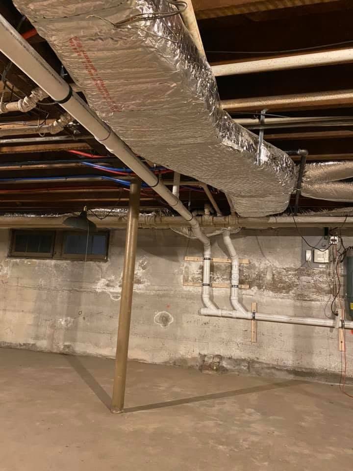 Basement with exposed pipes, ducts, and concrete walls under unfinished ceiling, with a support post. Basement with exposed pipes, ducts, and concrete walls under unfinished ceiling, with a support post.