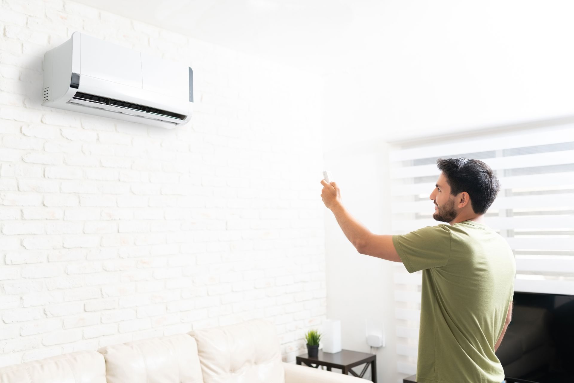 Person using a remote control to operate a wall-mounted ductless air conditioning unit.