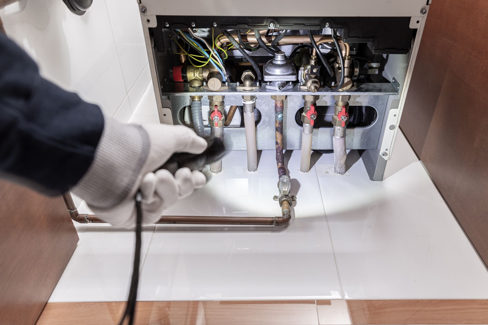 Technician inspecting and servicing a residential boiler with exposed pipes and valves.