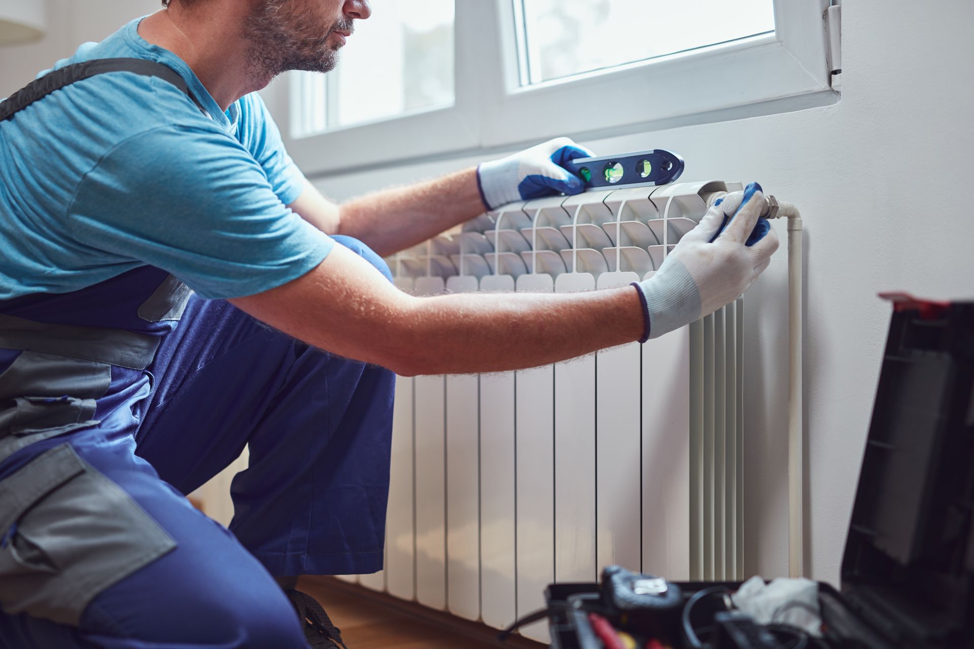 Technician using a level while installing or adjusting a wall-mounted home radiator.