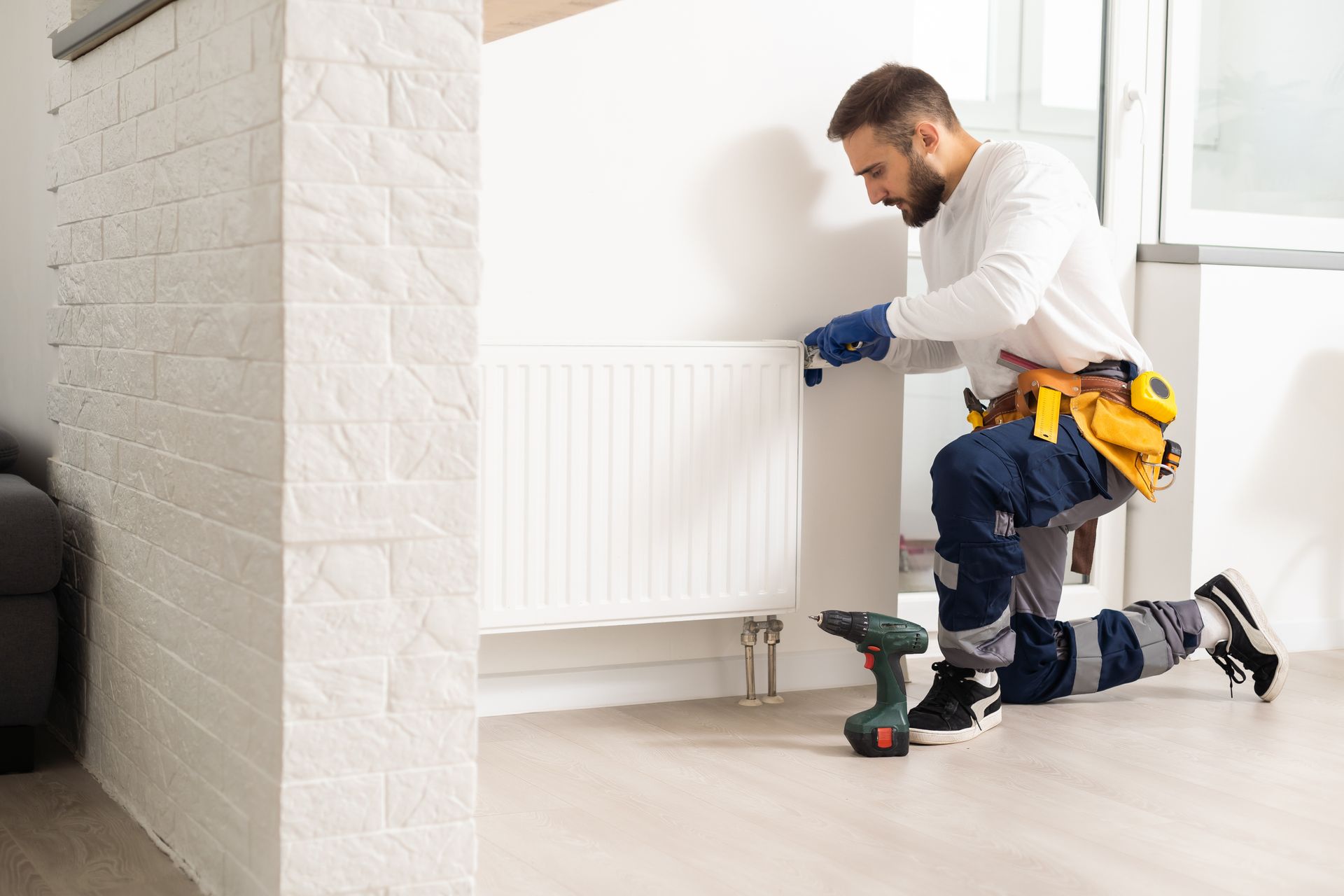 Technician installing or adjusting a wall-mounted home radiator with tools. Technician installing or adjusting a wall-mounted home radiator with tools.